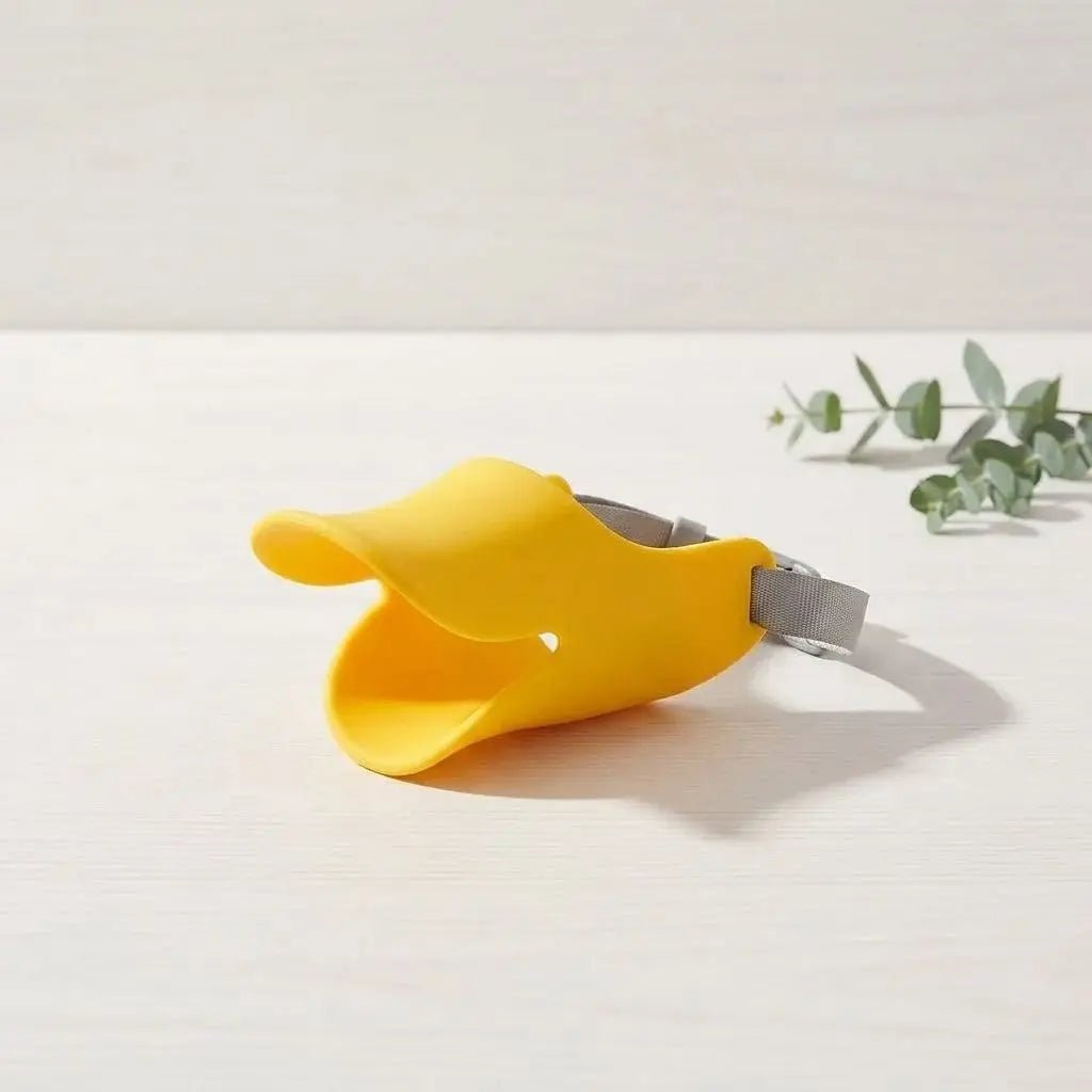 Muselière pour chien jaune avec sangle grise, proche d’une plante, indiquant un accessoire de sécurité pour chiens (Muselière Chien / Tinour).